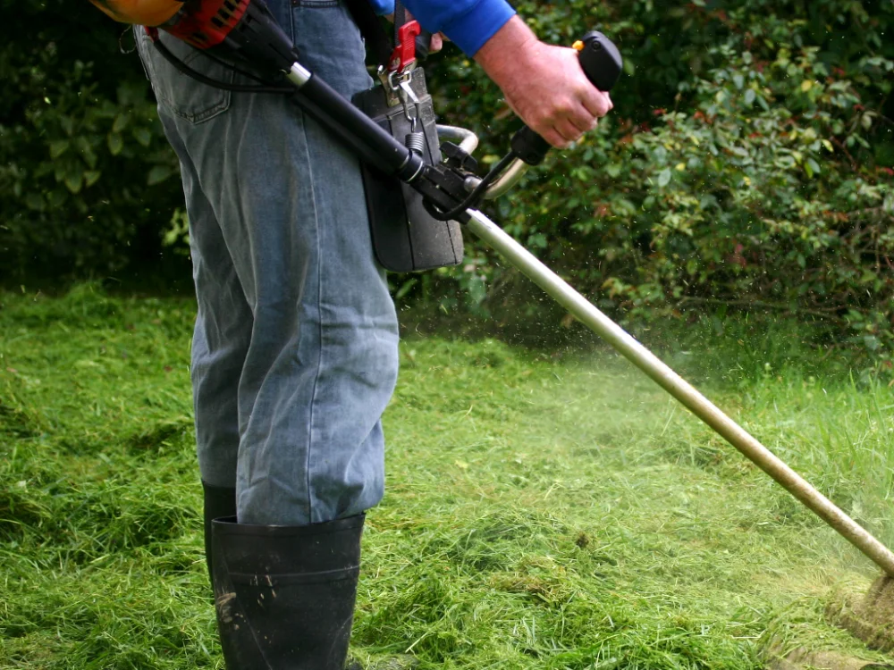 Grounds maintenance worker trimming grass with a brushcutter
